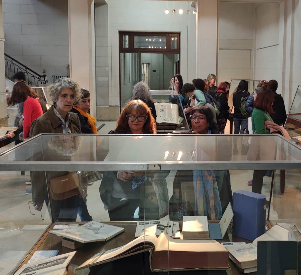 Fotografía del hall central de la biblioteca donde se puede ver la exhibición "Raros y Curiosos" y la observación de los participantes de la reunión sobre cada vitrina.
