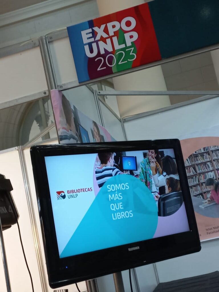 Fotografía del stand donde se puede ver la propuesta audiovisual que se propuso en el espacio, en la cual se puede ver el televisor con una de las imágenes del video que muestra la frase "somos más que libros".